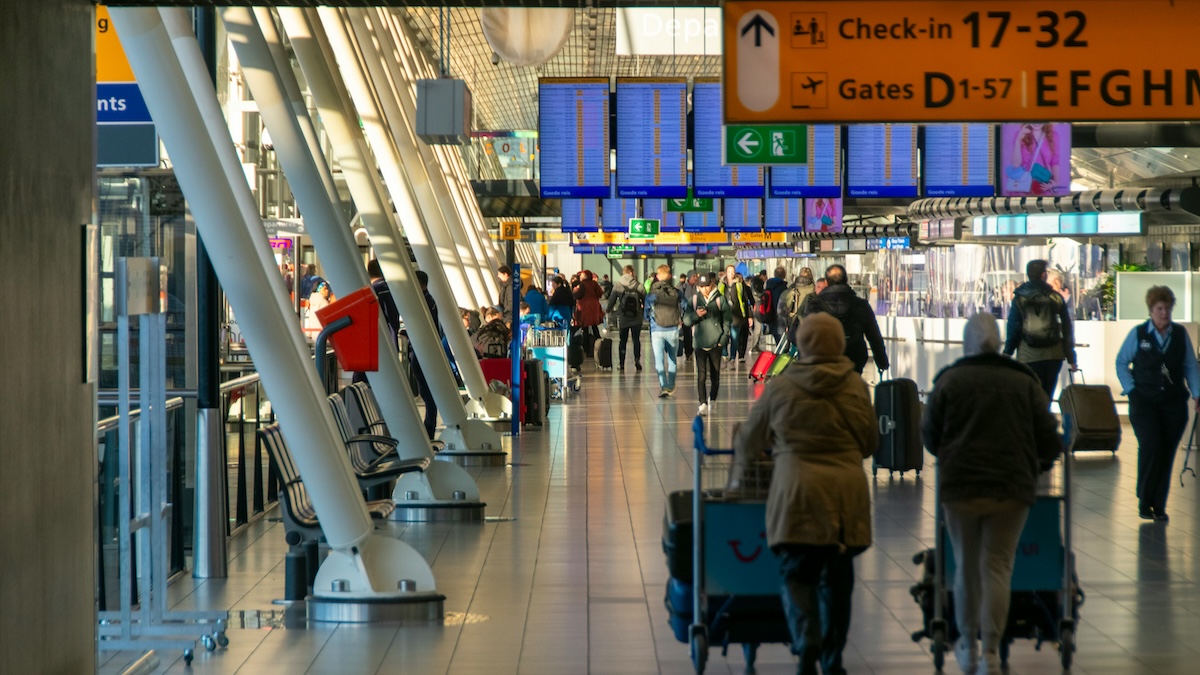 Travellers walking through an airport terminal beneath check-in and gate signage